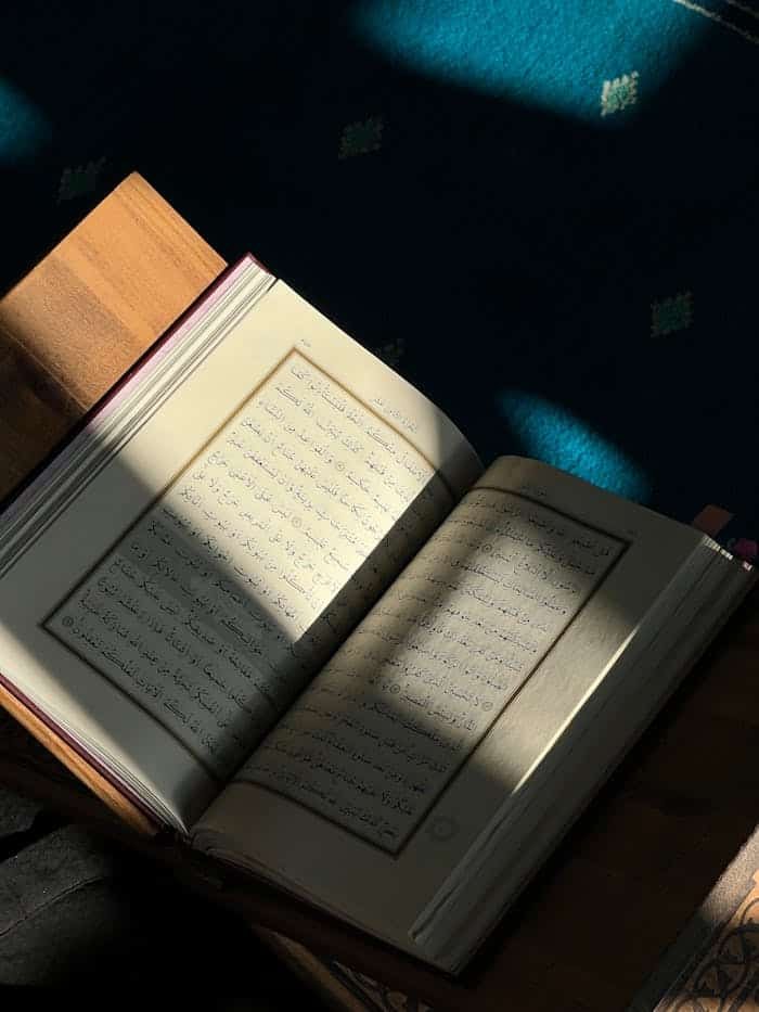 An open book with Arabic script is bathed in sunlight on a wooden table.