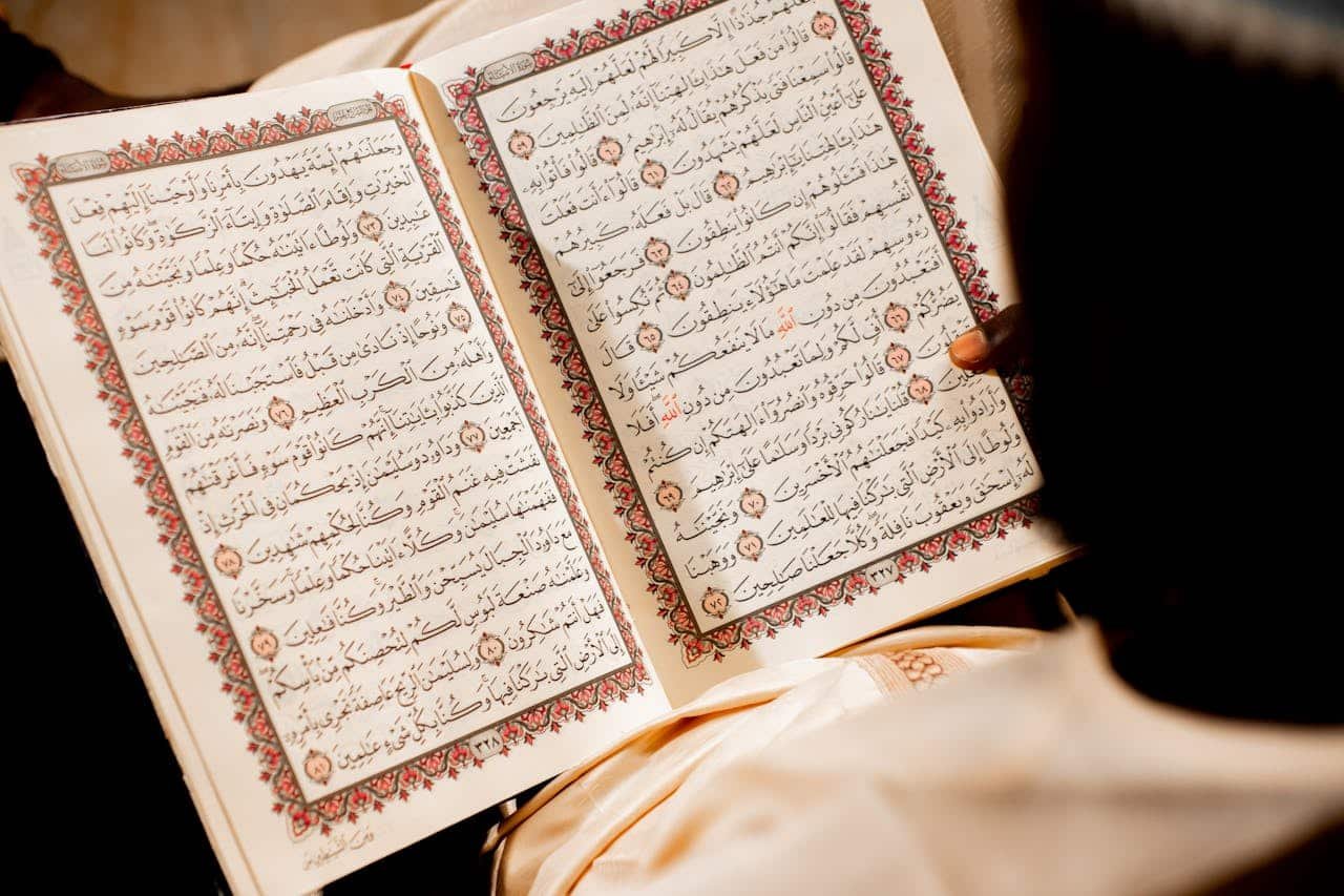 about-us A person reading an open Quran, focusing on religious text and spiritual reflection.